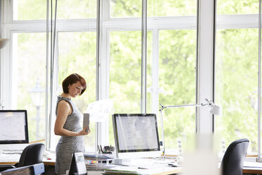 Female interior designer looking at swatch and blueprint in office - CUF12880