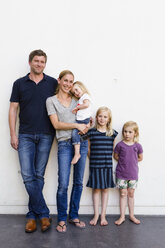 Porträt von Eltern und drei jungen Töchtern, die vor einer weißen Wand stehen - CUF12937