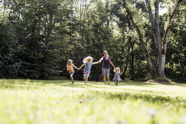 Mid adult woman and three young daughters holding hands and running in park - CUF12947