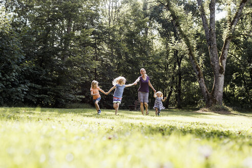 Mittlere erwachsene Frau und drei junge Töchter halten sich an den Händen und laufen im Park - CUF12947