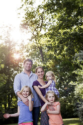 Porträt von Eltern und drei kleinen Töchtern in einem sonnenbeschienenen Park - CUF12952