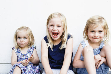 Porträt von drei jungen Schwestern, die vor einer weißen Wand sitzen - CUF12979