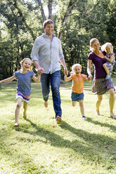 Paar, das mit seinen drei Töchtern im Park läuft und sich an den Händen hält - CUF12984