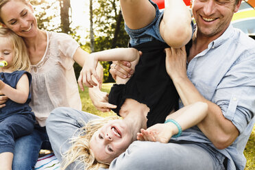 Father turning daughter upside down at family picnic in park - CUF12989