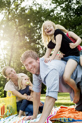 Father giving daughters piggyback at family picnic in park - CUF12990