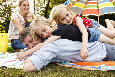 Zwei Töchter liegen auf dem Vater beim Familienpicknick im Park - CUF12991