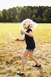 Girl waving bubble wand and making bubbles in park - CUF12996