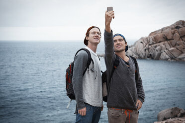 Junge Männer vor dem Meer, die mit ihrem Smartphone ein Selfie machen und dabei lächeln, Costa Smeralda, Sardinien, Italien - CUF13023