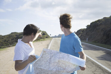 Young men on road holding map, looking over shoulder pointing, Costa Smeralda, Sardinia, Italy - CUF13026