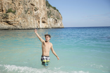 Junger Mann im Meer mit erhobenem Arm und lächelnder Kamera, Golfo di Orosei, Sardinien, Italien - CUF13043