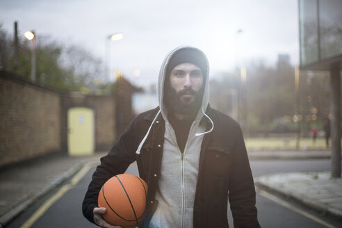 Porträt eines mittleren erwachsenen Mannes auf der Straße, der einen Basketball hält - CUF13075