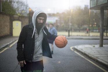 Mittlerer erwachsener Mann, der die Straße entlang geht und einen Basketball prellt - CUF13090