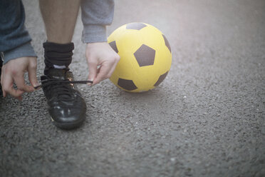 Junger Mann beim Binden von Schnürsenkeln, neben ihm ein Fußball, tiefer Ausschnitt - CUF13096