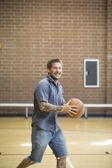 Tätowierter Mann hält Ball beim Üben auf dem Basketballplatz - ISF02135