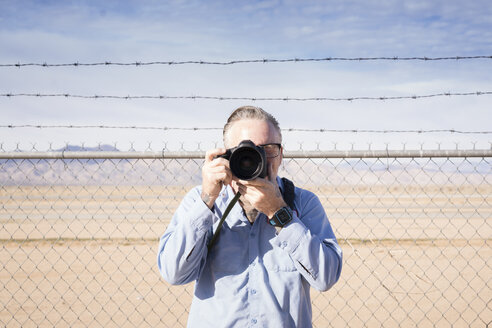 Photographer in front of barbed wire fence in desert taking photograph, California, USA - ISF02150