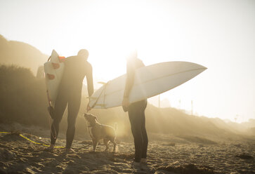 Surfer mit Hund im Sonnenlicht halten Surfbretter am Strand, Malibu, Kalifornien, USA - ISF02159