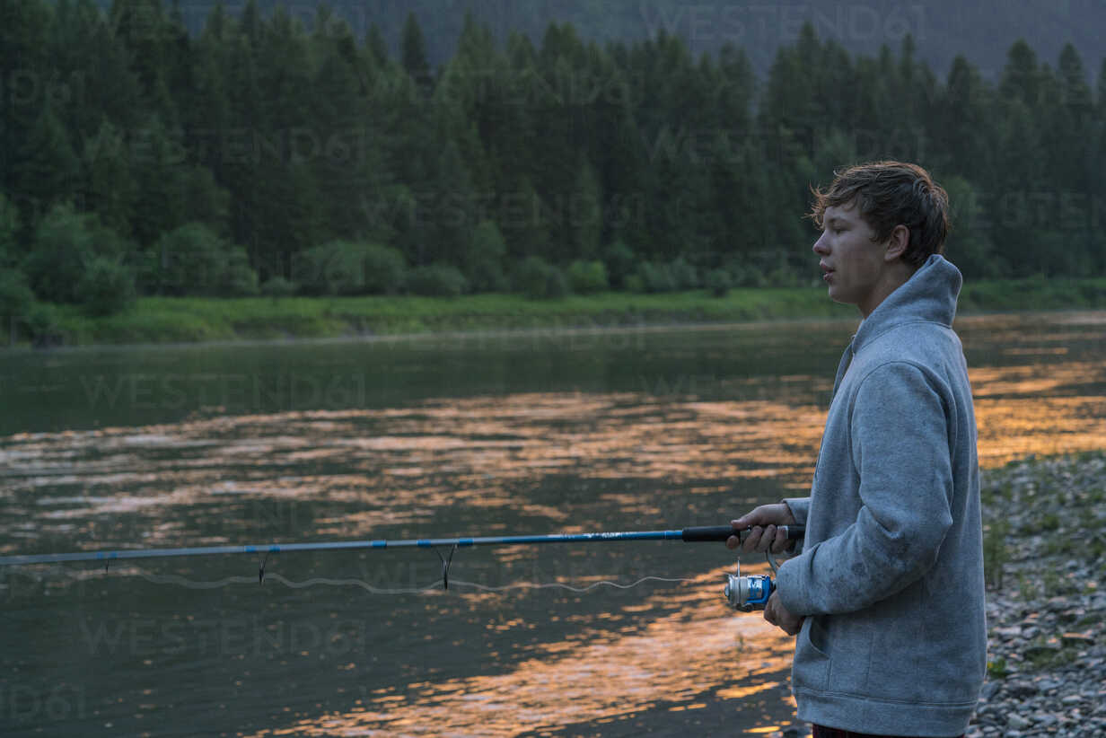 Teenage boy fishing in river at sunset, Washington, USA stock photo