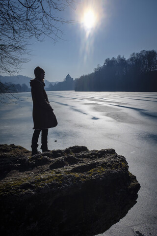 Frau am Seeufer im Winter in der Sonne stehend, lizenzfreies Stockfoto