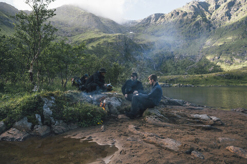 Norwegen, Lofoten, Moskenesoy, Junge Männer sitzen am Lagerfeuer am Agvatnet See, lizenzfreies Stockfoto