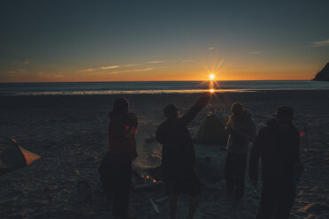 Norway, Lofoten, Moskenesoy, Young men standing at Kvalvika Beach at sunset - GUSF00795
