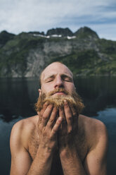 Mann wäscht seinen Bart an einem See mit geschlossenen Augen - GUSF00799