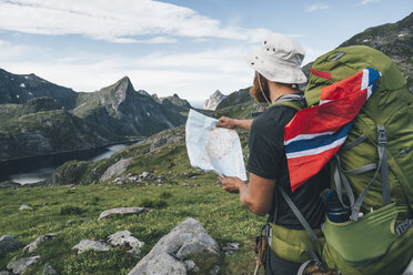 Norway, Lofoten, Moskenesoy, Man with backpak and Norwegian flag holding map - GUSF00808