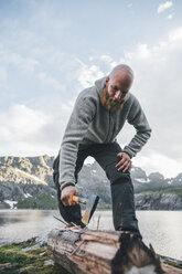 Norwegen, Lofoten, Moskenesoy, Junger Mann beim Holzhacken - GUSF00814