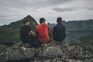 Norwegen, Lofoten, Moskenesoy, Drei junge Männer sitzen auf einem Felsen und blicken über den Kjerkefjord - GUSF00822