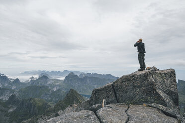 Norway, Lofoten, Moskenesoy, Young man standing at Hermannsdalstinden, looking over Kjerkefjord - GUSF00831