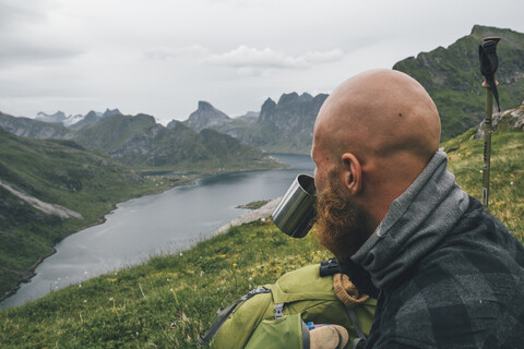 Norwegen, Lofoten, Moskenesoy, Mann schaut auf Aussicht, trinkt aus Zinnbecher, lizenzfreies Stockfoto