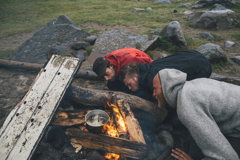 Norwegen, Lofoten, Moskenesoy, Drei Männer schüren die Flammen eines Lagerfeuers am Bunes Strand - GUSF00846