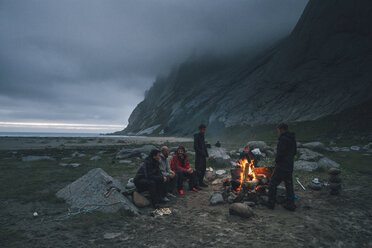 Norway, Lofoten, Moskenesoy, Group of young men sitting at a campfire at Bunes Beach - GUSF00849