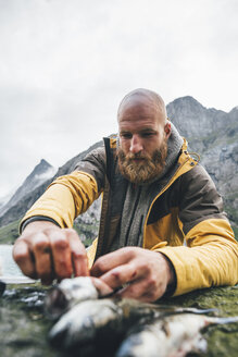 Norwegen, Lofoten, Moskenesoy, Junge Männer säubern fangfrischen Fisch am Strand von Horseid - GUSF00865