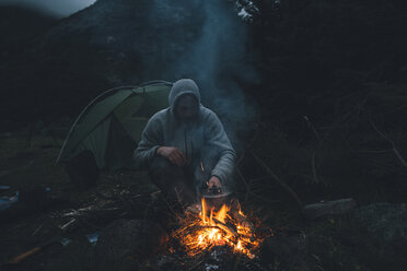 Norway, Lofoten, Moskenesoy, Young man sitting at camp fire - GUSF00871