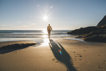 Norway, Lofoten, Moskenesoy, Man walking into the sun at Kvalvika Beach - GUSF00889