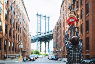 USA, New York, New York City, Father playing with baby in Brooklyn with Manhattan Bridge in the background - GEMF02002