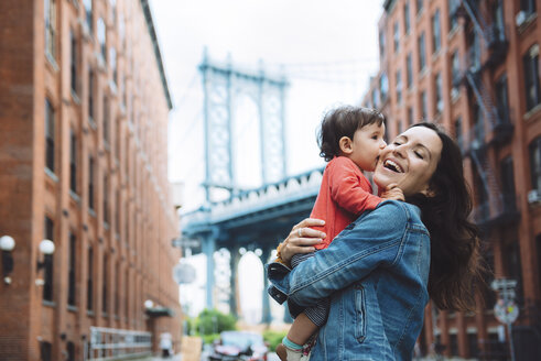USA, New York, New York City, Baby küsst Mutter in Brooklyn mit Manhattan Bridge im Hintergrund - GEMF02004
