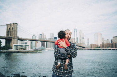 USA, New York, New York City, Vater umarmt ein Baby in Brooklyn mit Brooklyn Bridge und Manhattan im Hintergrund - GEMF02006