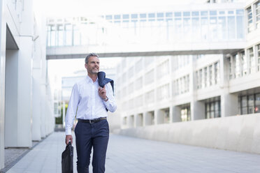 Businessman with laptop bag walking at courtyard of modern office buildings - DIGF04318