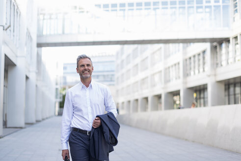Porträt eines lächelnden Geschäftsmannes, der im Innenhof eines modernen Bürogebäudes spazieren geht - DIGF04320