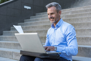 Porträt eines Geschäftsmannes, der auf einer Treppe sitzt und einen Laptop benutzt - DIGF04340