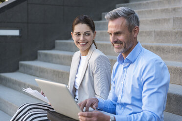 Two business people sitting side by side on stairs working together - DIGF04345