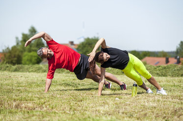 Couple doing side plank exercise on meadow - DIGF04355