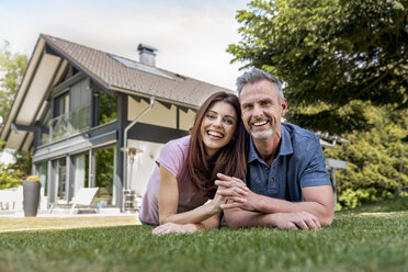 Portrait of happy couple lying in garden of their home - DIGF04370