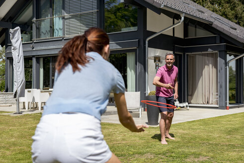 Glückliches Paar spielt mit einer Flugscheibe im Garten ihres Hauses - DIGF04377