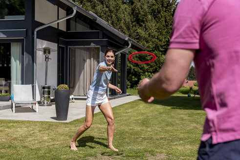 Glückliches Paar spielt mit einer Flugscheibe im Garten ihres Hauses - DIGF04378