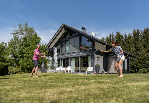 Glückliches Paar spielt mit einer Flugscheibe im Garten ihres Hauses - DIGF04379