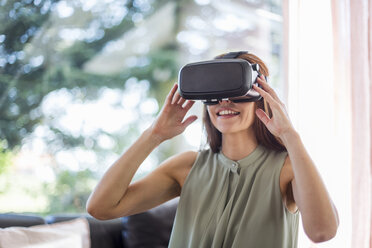 Smiling woman at home wearing VR glasses - DIGF04381