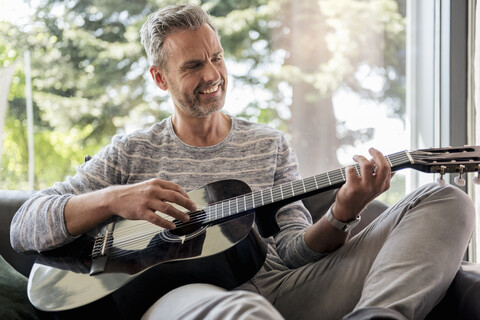 Glücklicher reifer Mann, der zu Hause auf der Couch liegt und Gitarre spielt, lizenzfreies Stockfoto