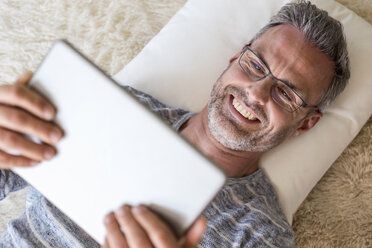 Mature man lying on pillow using a tablet - DIGF04391